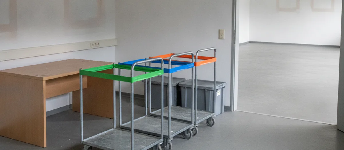 Mit Farbband markierte Rollcontainer und graue Aktenbehälter stehen abfahrbereit in einem geräumten Büro.